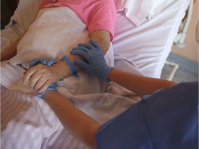 A nurs wearing protective gloves holds the hand of a patient.