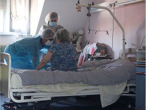 Laboratory staff, wearing protective suits and face masks, take a blood sample from a patient.