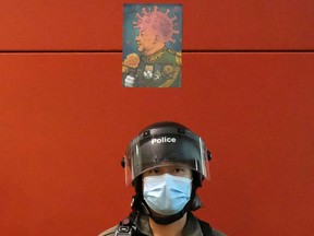 A defaced picture mocking Chinese President Xi Jinping and the coronavirus disease (COVID-19) is seen above a riot police wearing a face mask as officers disperse the crowd in a mall to avoid the spread of the coronavirus disease (COVID-19), in Hong Kong, China April 26, 2020.