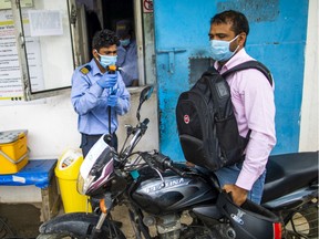 A security guard sprays a worker arriving on a motorcycle with disinfectant at the entrance to the factory of Ajit Industries Pvt., a manufacturer of industrial adhesive tapes and die cuts, in Sonipat district, Haryana, India, on Monday, Apr. 20, 2020.