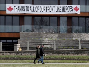 An unidentified couple walk near Dow's Lake and in front of a sign in praise of front-line health-care workers on Friday.