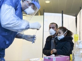 A medical staff member prepares to collect a sample from a man and his daughter at a COVID-19 testing centre set up in the European Parliament on May 12, 2020, in Strasbourg, eastern France.
