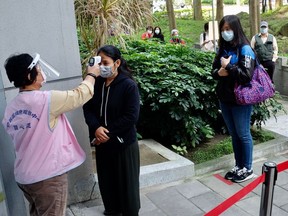 A masked resident has her temperature checked as people line up to buy face masks from vending machines at the Xinyi District Health Center in Taipei on April 14, 2020.