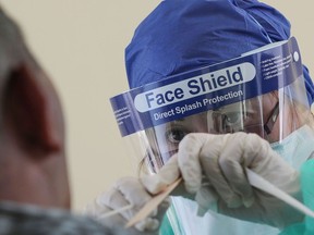 A health worker, wearing personal protective equipment, collects a swab sample.