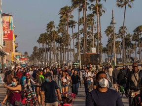 People walk at the boardwalk in Venice Beach during the first day of the Memorial Day holiday weekend amid the novel Coronavirus, COVID-19, pandemic in California on May 23, 2020.