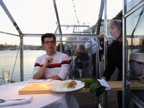 A server is seen with protective gear serving food on a table at a restaurant where they test servers providing drinks and food to models pretending to be clients in a safe "quarantine greenhouses" in which guests can dine in Amsterdam May 5, 2020.