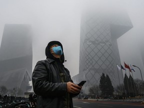 A Chinese man wears a protective mask as he stands near the CCTV building in fog and pollution during rush hour in the central business district on February 13, 2020 in Beijing, China.