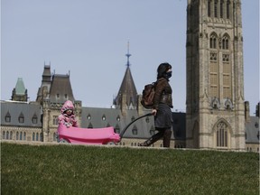 A woman wearing a protective mask pulls a wagon carrying a child along the grounds of Parliament Hill. The federal government must grapple with the future of international co-operation.