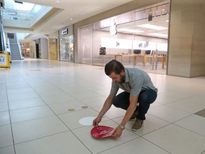 Justin Markey lays down social distancing stickers on the floors of the Bayshore Shopping Centre as it returned to business.