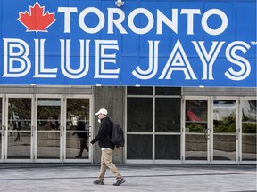 A man wearing a mask walks past the Toronto Blue Jays logo outside Rogers Stadium in Toronto in early May.