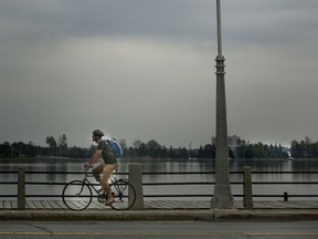 A man cycles along the bike path at Dow's Lake under overcast skies.