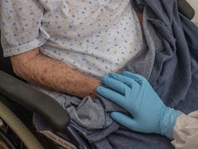 A health care nurse in personal protective equipment touches the hand of an older resident in COVID-19 quarantine  at a nursing home.