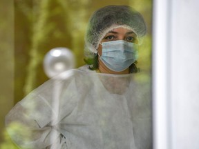 A nurse wearing a protective outfit and face mask looks out a window.