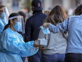 Staff from Park Extension COVID-19 testing centre hands surgical mask to a woman waiting in line in Montreal Thursday September 24, 2020. (John Mahoney / MONTREAL GAZETTE)