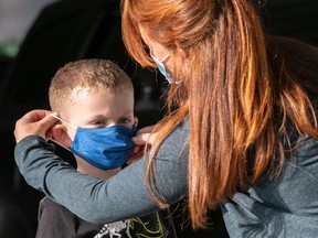 FILE: A teacher puts on a child's mask upon his arrival at school.