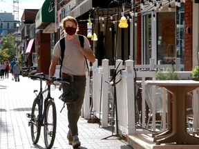 A man walks his bike past restaurant patios on Wellington Street.