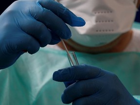 FILE PHOTO: A doctor, wearing a protective suit and a face mask, holds a test tube after administering a nasal swab at a COVID-19 testing site.