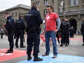 A man wearing a t-shirt adorned with a Swiss cross is controled by the police during a protest against the new measures against the coronavirus in front of the House of Parliament on October 18, 2020 in Bern. - The Swiss government said on October 17 it was making the wearing of masks in indoor public spaces compulsory under new measures introduced after a "worrying" rise in coronavirus infections. More than 15 people in public would also be banned under the rules to take effect on Monday, while service in restaurants and bars would be restricted to seated customers only.