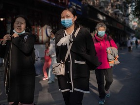 A woman wearing a face mask walks past restaurants on a street in Beijing on October 19, 2020.