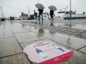 People shelter from the rain under their umbrellas as they walk past a partly damaged sticker of the Swedish healthcare services on a pavement to instruct people to follow the 2 meters rule on October 22, 2020, during the novel coronavirus COVID-19 pandemic.