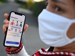 A woman wearing a face mask holds a smartphone showing the new "TousAntiCovid" application in Rennes, western France, on October 22, 2020, as several departments were put in "maximum alert" and new curfew measures put in place in order to curb the spread of the Covid-19 (the novel coronavirus). - The "StopCovid" contact tracing application, which has been controversial and little used since its release on June 2, has been relaunched on October 22 in a new form and renamed "TousAntiCovid".