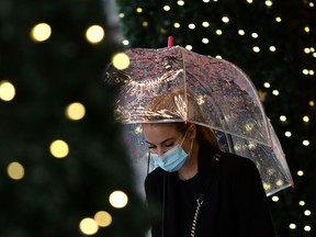A pedestrian wearing a face mask shelters under an umbrella.