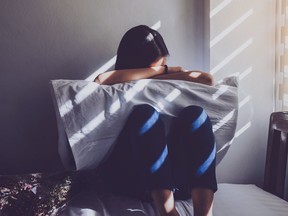 FILE: A woman sits alone on her bed.