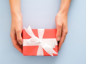 Female's hands holding red gift box with white ribbon bow on pastel blue background. Christmas, New Year, Valentine's day and birthday concept. Minimal flat lay style composition, top view, overhead