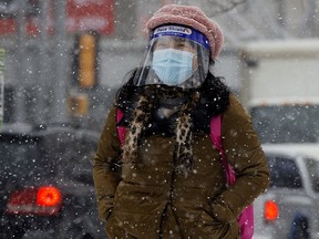 A pedestrian wearing a COVID-19 mask and face shield makes their way through the falling snow.