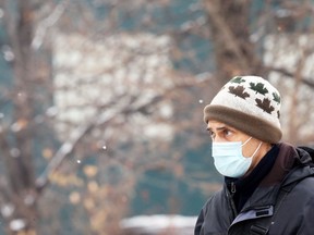 A man wearing a mask watches snowflakes fall.
