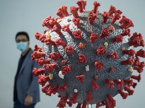 FILE: A man walking past a model of the coronavirus.