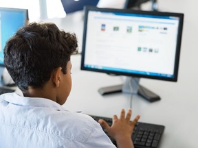 A stock image of a young boy using a desktop computer in a school library.