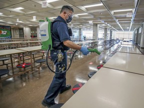 Caretaker Paul Saletnig disinfects tables in the cafeteria at John F. Kennedy High School in November. High school students will stay home for one more week to take part in online classes. They will return to class on Jan. 18.