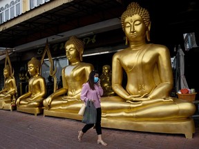 A woman wearing a face mask walks past golden Buddha statues in Bangkok on Jan. 5, 2021. Secular Buddhist teachings can help us approach the pandemic effectively.