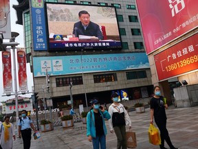 Big Brother is watching: People wearing face masks walk under a giant screen showing news footage of Chinese President Xi Jinping in Beijing.