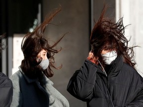 Pedestrians, wearing protective masks against COVID-19, stand in strong wind.