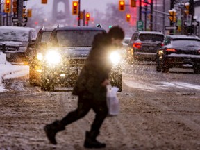 A pedestrian runs across Elgin Street with snow falling.