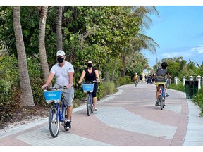 Tourists wear masks as they bike along the beach in Miami in December. The pandemic has separated Canada's "snowbirds" into two camps: those staying home and those heading to Florida no matter the cost, financial or otherwise.