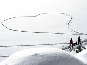 People and their dog walk near a heart shaped in the snow.