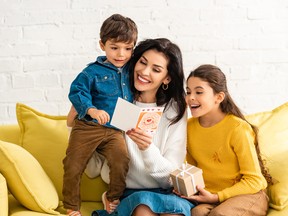 happy woman holding mothers day card and embracing son, while daughter holding gift box