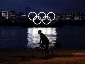A man rides his bicycle in front of the Olympic rings at the Odaiba waterfront in Tokyo on April 12, 2021.
