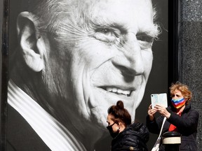 A woman takes a selfie photograph outside a supermarket with a poster featuring Britain's Prince Philip, Duke of Edinburgh in the window, in the High Street of Windsor, west of London, on April 16, 2021.