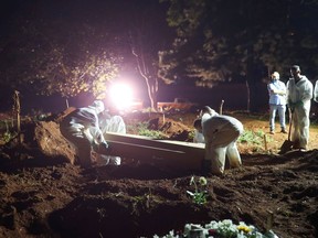 FILE: Gravediggers wearing protective suits carry a coffin of a 32-year-old man who died from the coronavirus disease (COVID-19) as spotlights illuminate the graves during night burials at Vila Formosa cemetery in Sao Paulo, Brazil, March 30, 2021.