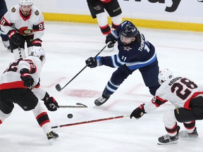 Nate Thompson #11 of the Winnipeg Jets gets off a shot under pressure from  Nikita Zaitsev #22 and Connor Brown #28 of the Ottawa Senators during third period NHL action on May 8, 2021 at Bell MTS Place in Winnipeg.