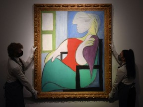 In this file photo taken on April 22, 2021 gallery workers display an artwork titled 'Femme assise près d'une fenêtre (Marie-Thérèse)' by Spanish painter Pablo Picasso during a photocall at Christies auction house in central London. - Pablo Picasso's "Woman sitting by a window (Marie-Therese)" sold Thursday for $103.4 million at Christie's in New York, the auction house said.