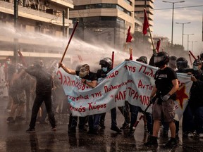 Pro-palestinians supporters hold placards and wave flags while being sprayed by water canons during a demonstration in solidarity with the Palestinians called over the ongoing conflict with Israel, outside the Israeli embassy, in Athens on May 15, 2021.