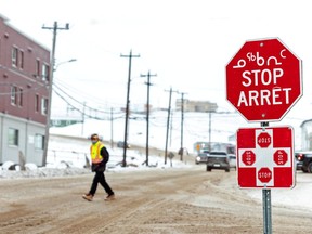 FILE PHOTO: A man wearing a mask to help slow the spread of coronavirus disease (COVID-19) passes a stop sign written in English, French and Inuktitut as the territory of Nunavut.