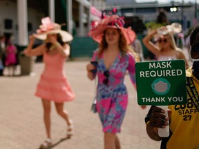 Maskless spectators walk next to a staff members carry a sign that reads Mask Required at Churchill Downs on the running of 147th Kentucky Derby in Louisville, Kentucky, U.S. April 30, 2021.