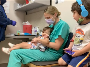 Sloan Bui, age 14 months, and Christian Bui, age 3, wait with their mother, Erin Biro, at the hospital to get their shots.