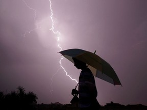 FILE: A pedestrian walks with an umbrella as lightning strikes.